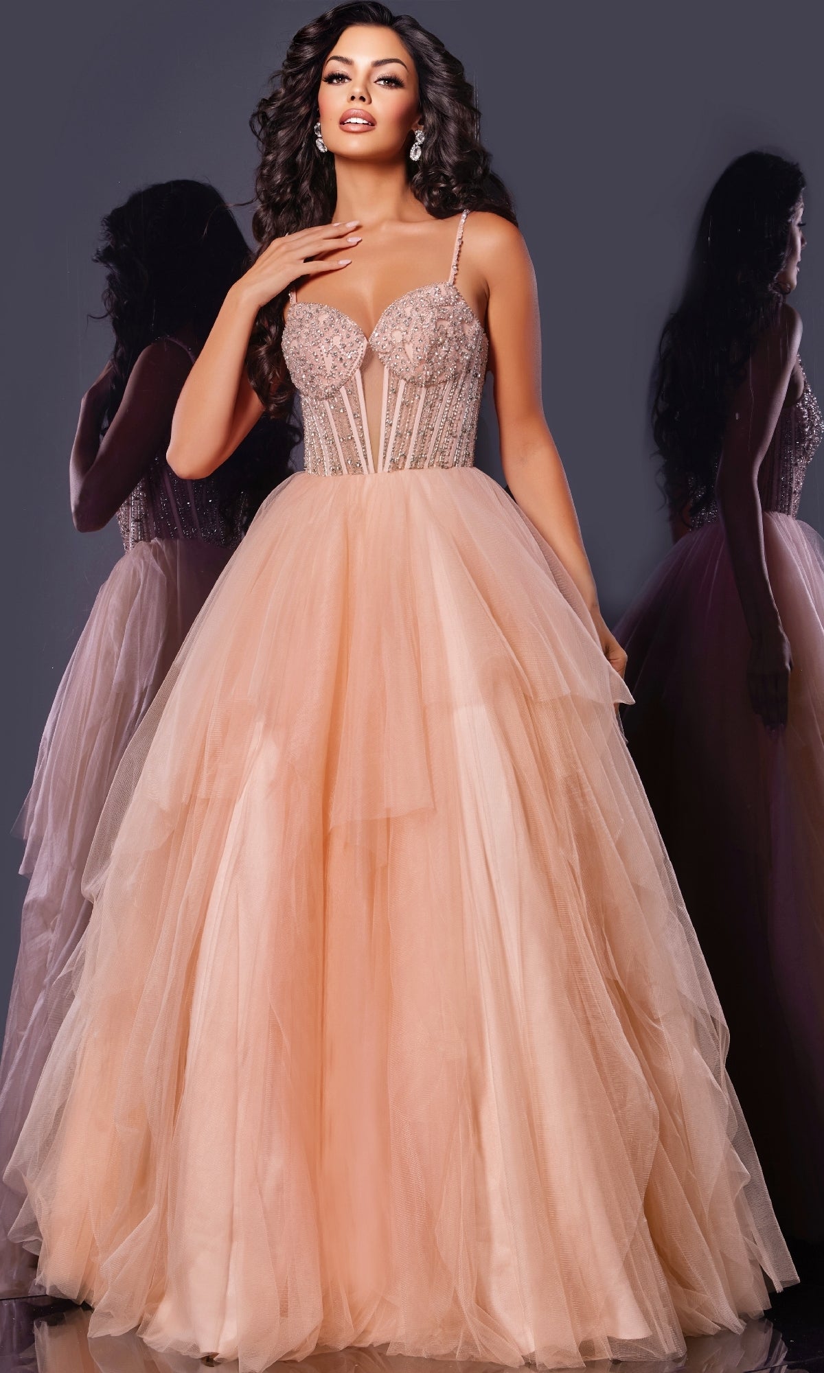 A woman models the Jovani 43254 long prom dress in blush pink, featuring an embellished corset bodice and voluminous tulle skirt, standing against a dark background with her reflection visible.